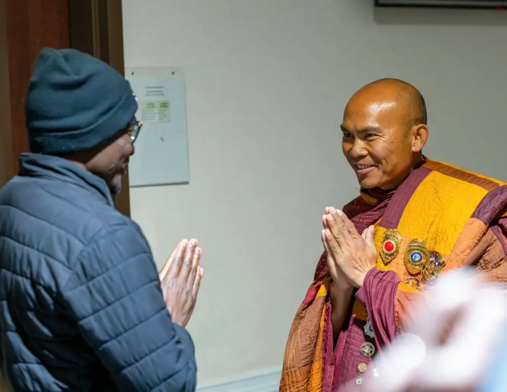 Reverend Edward Tembo and a Buddhist monk face one another with hands in prayer during the Walk for Peace visit at Our Lady of the Rosary Catholic Church.